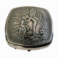 Top view of the powder compact showing embossed fairy design and floral motifs in Art Nouveau style.