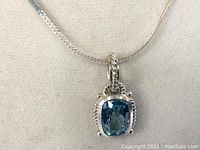 Close-up image showing the pendant's blue cushion-cut gemstone with silver rope and bead detailing on the sides, hanging from the chain.