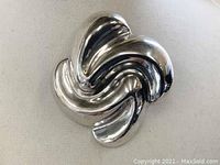Front view of heavy sterling silver swirl pendant/pin showing polished curved shapes and loop for pendant wear.