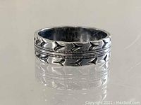 Front view of wide silver band ring showing decorative arrow and beaded patterns on edges and center.