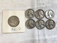 Obverse view of six Washington quarters and one in holder labeled 1961-D, showing George Washington's profile and dates visible on coins.