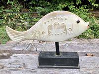 Full view of ceramic fish sculpture showing side profile, decorative incised and impressed patterns on body, black wire spines, and black ceramic base.