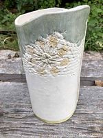 Front view of asymmetrical vase showing abstract sunflower design with sage green glaze top and white body.