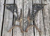 Pair of ornate cast iron Victorian school desk frames laid on weathered wood surface, showing complete sides with decorative ironwork and footprint.