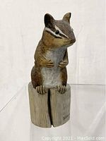 Front view of small carved wooden chipmunk sitting on a log base, painted in natural colors with visible fur and facial detail.