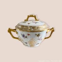 Porcelain sugar dish with lid shown against plain pale background emphasizing gold handles, floral decoration, and shape.