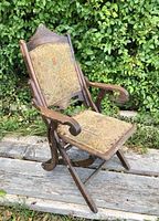 Front angled view of antique Eastlake folding armchair showing carved walnut frame and tapestry fabric upholstery.