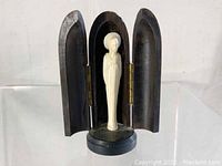 Small carved white Virgin Mary statuette on a round base inside a three-paneled, hinged dark wood case, opened