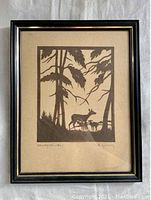 Full frontal image of the framed silhouette cut paper artwork of deer in forest, showing the frame and art piece in entirety.