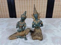 Overview of both antique Thai Buddhist figures side by side on fabric surface with bamboo screen background.