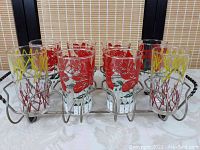 Front view of all 8 glasses arranged in metal stand showing red and yellow designs