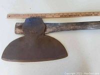 Close up angled view of the broad axe blade and partial wooden handle, showing wear and size scale with ruler.