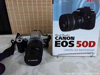 Photography book titled 'David Busch's Canon EOS 50D Digital SLR Photography' standing upright next to stuffed Canon camera with lens caps on