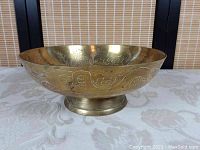 Front side view of the Chinese brass footed bowl showing detailed dragon and cloud engravings and the round base.