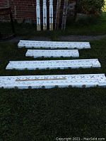 Four white painted wooden fretwork panels on grass in front of brick wall