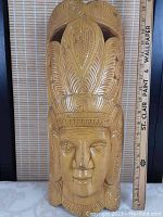 Full front view of the carved wooden mask with a measuring ruler behind showing its height at about 18.5 inches and width about 8.5 inches.