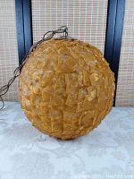 Spherical amber/gold textured fabric shade hanging lamp shown on a table with original dark metal chain and pull string cable, lamp unlit.