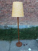 Full view of the teak floor lamp with woven fabric shade placed outdoors showing height and overall condition.
