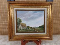 Full front view of the original oil painting in its ornate gold frame displayed on a wooden easel against a wicker background