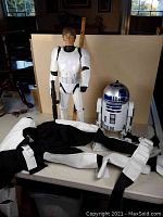 Full view of 31" Luke Skywalker figure wearing stormtrooper armor with black bodysuit, holding black blaster rifle; R2-D2 unit and costume pieces laid out on table