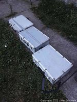 Three closed metal Vanguard cases placed on grass and concrete, showing their size and shape.