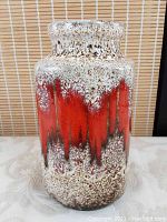 Front view of vintage ceramic vase with bright orange melting glaze effect on speckled white and brown background, flared rim visible.