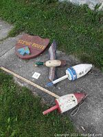 Photo showing all four items: wooden scenic route sign, painted flying duck, two wooden buoys on pavement with grass