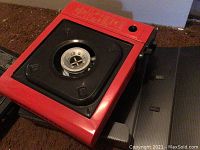 Red single burner camp stove with square burner platform, visible controls and feet see photo 1