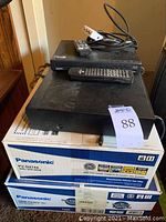 Two sealed Panasonic boxes (PV-D4744 and DMR-ES35V) with two unboxed players stacked on top