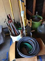 Photo of yellow-handled loppers, hand saws, and coiled garden hoses in a box