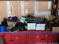 View of red shelving with various gardening and yard supplies, boxes, bags, and tools stored atop and inside.