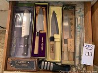 Drawer containing multiple boxed Japanese knives, a Fine Edge Pro santoku, ACME oil stone, manual sharpener and cutlery
