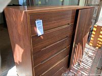 Front view showing five drawers and right-side hinged door, wood grain finish, tag with lot number.