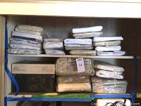 Shelf showing multiple wrapped sheets in beige, tan, and white solid colors, thermal blankets, and a bedspread, all new in packaging.