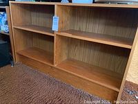 Pair of short wood bookshelves with two shelves each, shown on carpeted floor with minor dust and wear visible.