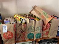 Several paper bags containing boxes of sandwich bags, storage bags, aluminum foil, and cleaning supplies placed side by side on a shelf.