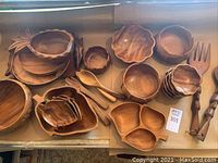 Full assortment of wooden Polynesian style serving bowls, platters, and utensils made from monkey pod wood arranged on tabletop.
