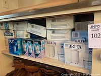 Shelf with multiple boxes of Pur and Brita brand faucet water filtration systems and replacement cartridges, mostly unopened.