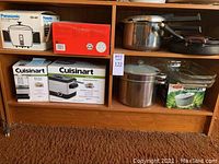 Photo showing various kitchen appliances and cookware arranged on shelves, including boxed Cuisinart appliances, Pyrex glass dishes, pots and pans.
