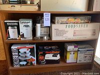 Full shelf displaying all boxed kitchen appliances including coffee grinders, bowl set, sharpener, can opener, food processors, and vacuum sealer.
