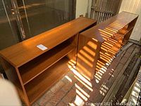 Two matching low bookshelves side by side on brick floor under partial shade