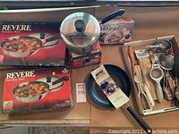 Photo showing boxed Revere stainless steel covered skillets, Meyer Avalon skillet, assorted utensils in box, and grater in box