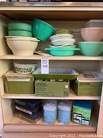 Full shelving display of lot contents showing plastic bowls, boxed Pyrex sets, glass dishes and Tupperware