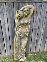 Full view of vintage gold tone relief wall sculpture showing woman standing with jug on shoulder against a wooden fence.