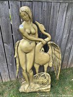 Full front view of the vintage gold fiberglass Leda and the Swan sculpture standing against a wooden fence.