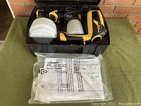 Top view of the open black carrying case showing the yellow and black Wagner Flexio paint sprayer with attached paint containers and sealed instruction manual.