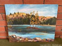 Front view of the oil painting showing lake, trees with fall foliage, rocks in foreground, and blue sky