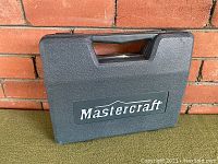 Closed dark grey Mastercraft carrying case with handle and logo on front.