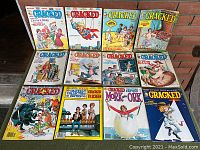12 vintage Cracked magazines arranged in two rows on a wooden surface, colorful illustrated covers, varying condition.