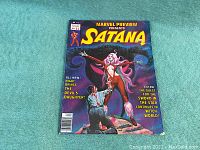 Front cover showing full painted illustration of Satana with outstretched arms and kneeling man at her feet against a night sky